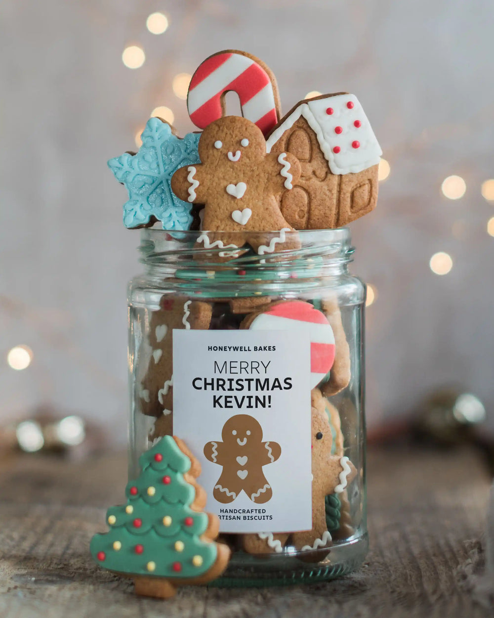 Honeywell Bakes Jar of Gingerbread Men Biscuits - A clear glass jar filled with decorated Christmas gingerbread cookies, topped with a gingerbread man, candy cane, snowflake, and house cookie, and with a green tree cookie leaning against the front. 