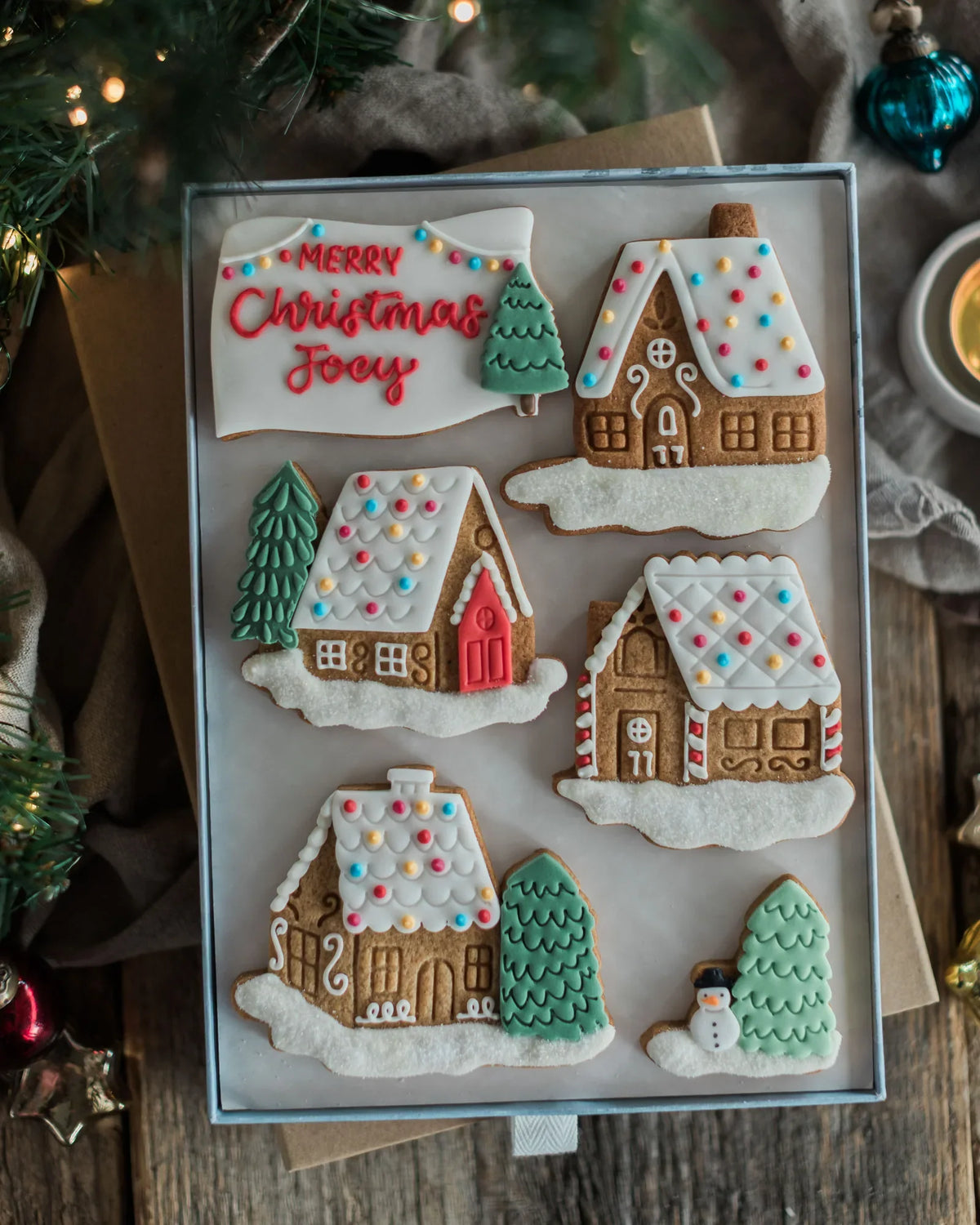 Honeywell Bakes Personalised Christmas Village Biscuit Gift - A set of six decorated Christmas gingerbread cookies arranged on a square tray. The cookies include gingerbread houses with colourful icing roofs and a personalised biscuit
