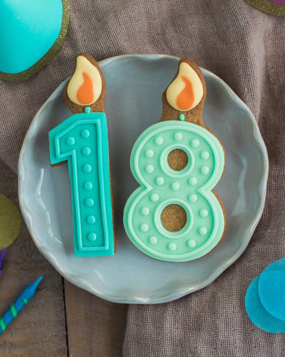 Honeywell Bakes 18th Birthday Biscuits - Two cookies shaped like number 18 and candles on a plate with a brown background