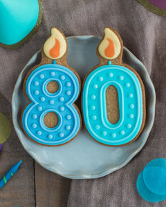 Honeywell Bakes 80th Birthday Biscuits - Two cookies shaped like the number 80 with blue icing and candle decorations on a gray plate.