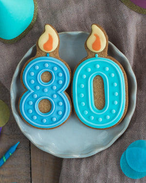 Honeywell Bakes 80th Birthday Biscuits - Two cookies shaped like the number 80 with blue icing and candle decorations on a gray plate.