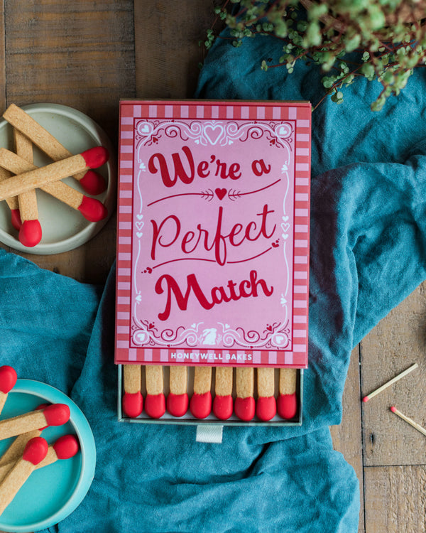 Honeywell Bakes A Perfect Match - A Perfect Match Biscuit Gift - Matchbox set of shortbread cookies with 'We're a Perfect Match' text on a wooden surface with blue fabric and shortbread matches.