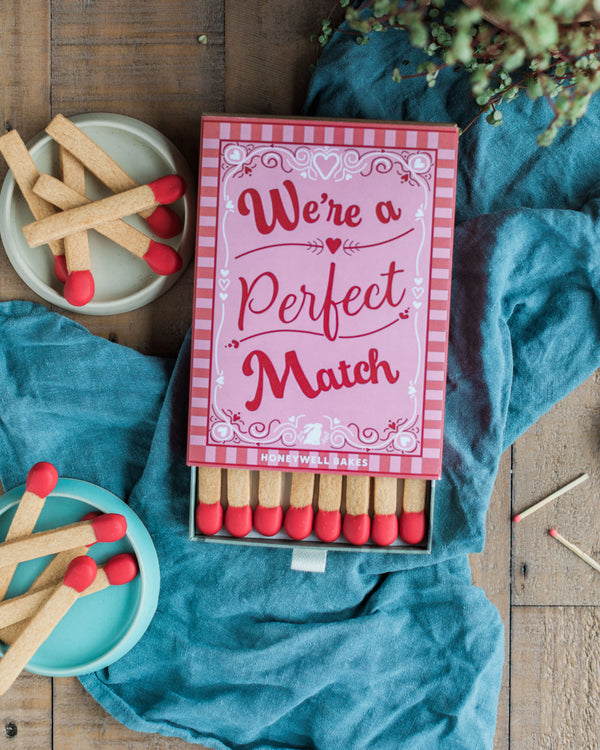 Honeywell Bakes A Perfect Match - A Perfect Match Biscuit Gift - Shortbread Cookie Matches with a pink box labeled 'We're a Perfect Match' on a wooden surface with blue fabric.