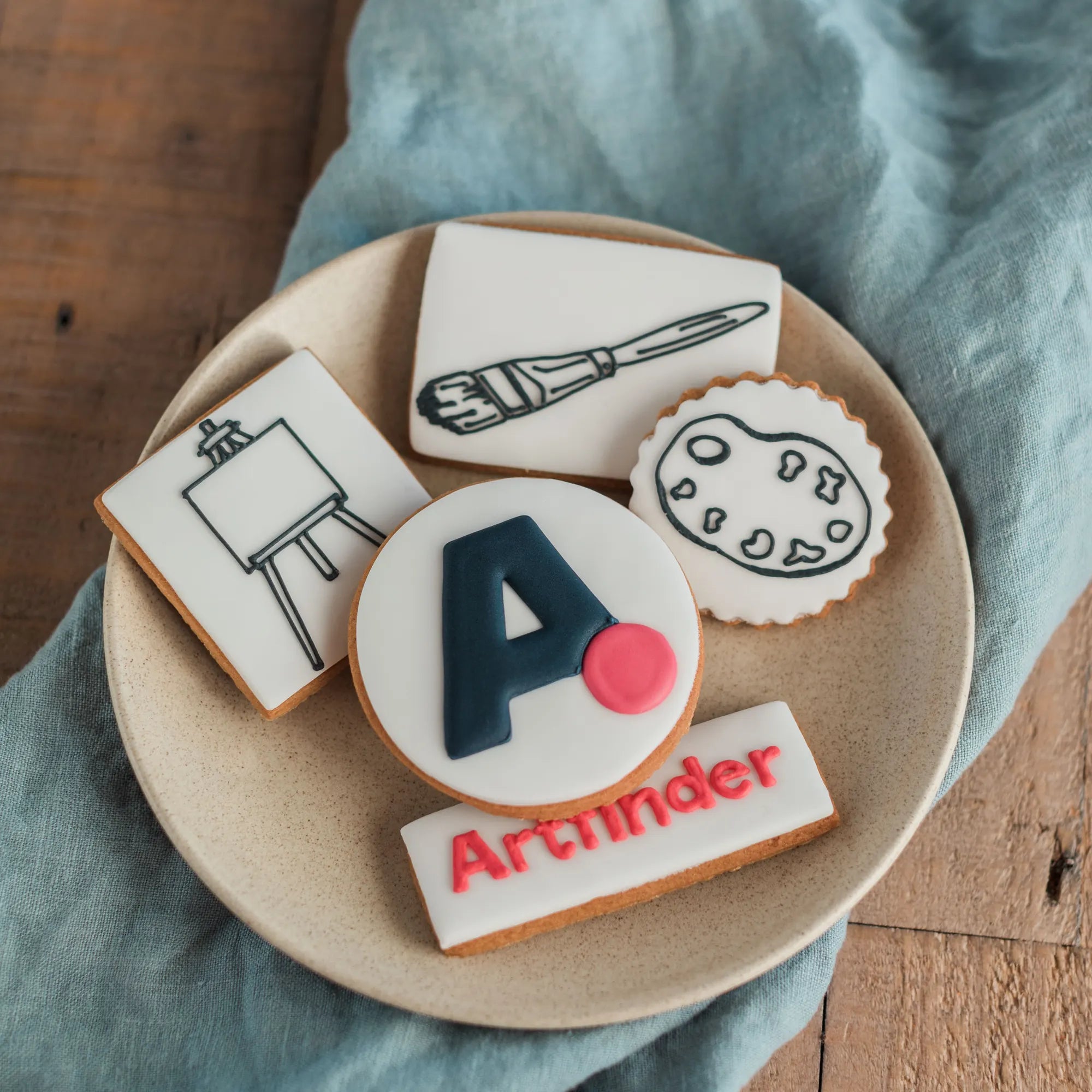 Honeywell Bakes logo biscuit gift, A set of five hand iced sugar cookies featuring art illustrations of an easel, paintbrush, palette, and logo biscuit.