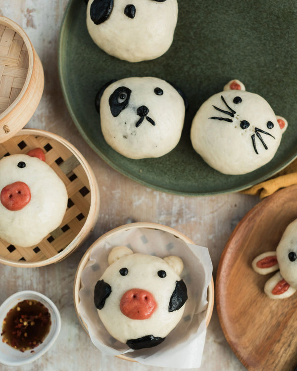 Honeywell Bakes Bao Buddies Baking Kit -  Various animal-shaped bao buns on a table with a green plate and wooden baskets.