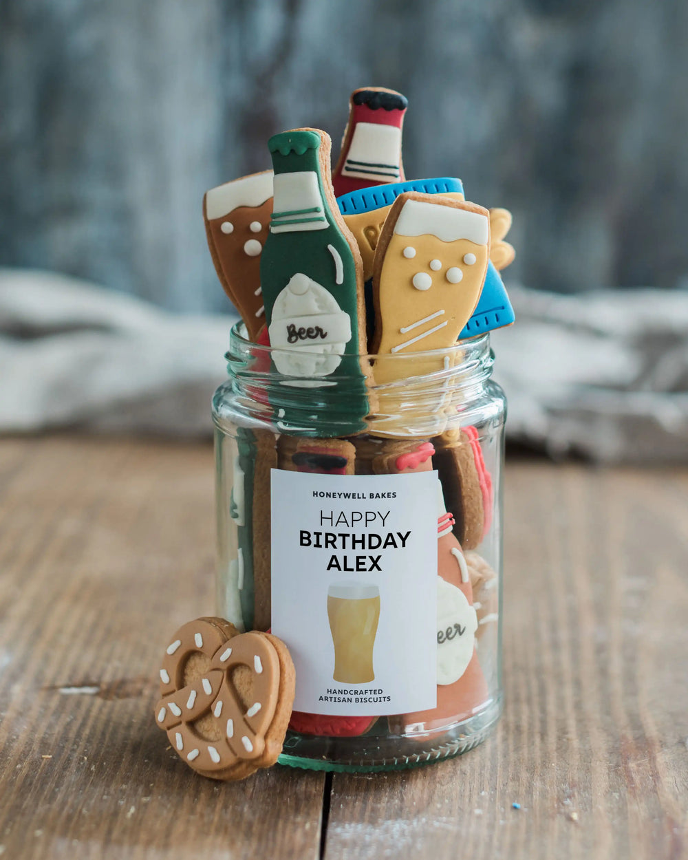 Honeywell Bakes Beer Lover’s Biscuit Jar - Jar of beer themed cookies including bottles and glasses with a label on a wooden surface.