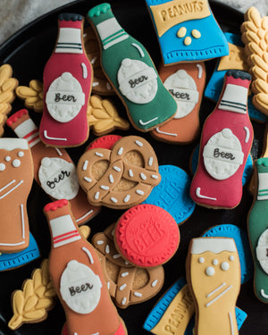 Honeywell Bakes Beer Lover’s Biscuit Jar - Assorted cookie shapes including bottles, pretzels, and peanuts on a black plate.