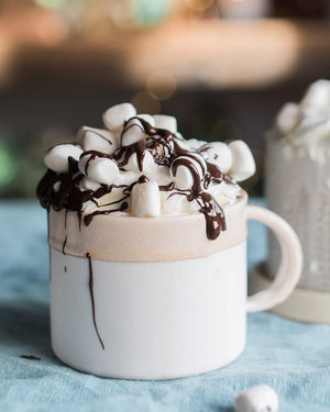 Honeywell Bakes Belgian Hot Chocolate Kit - White mug filled with hot chocolate, topped with marshmallows and chocolate drizzle on a blue surface.