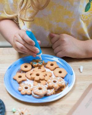 Honeywell Bakes Biscuit Jewellery Craft Kit - Child decorating cookies with a piping tube on a wooden table.