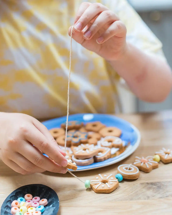 Honeywell Bakes Biscuit Jewellery Craft Kit - Child's hands playing with a string of cookies on a wooden table.