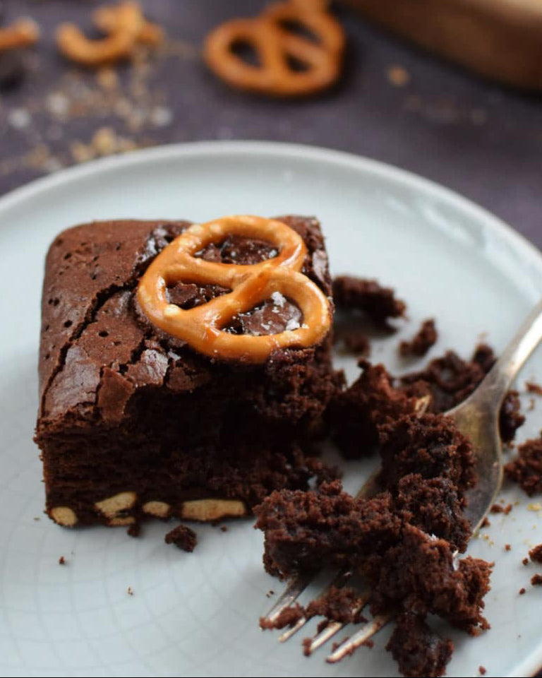 Chocolate brownie baking kit with pretzels on a plate with a fork, on a dark surface.