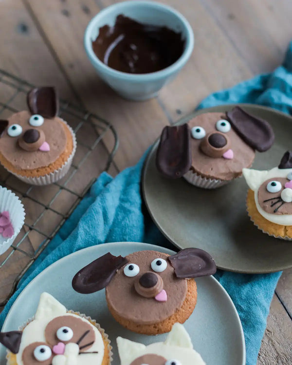 Honeywell Bakes Cat & Dog Cupcake Baking Kit - Cupcakes decorated to look like dogs on a wooden table with a bowl of chocolate frosting.