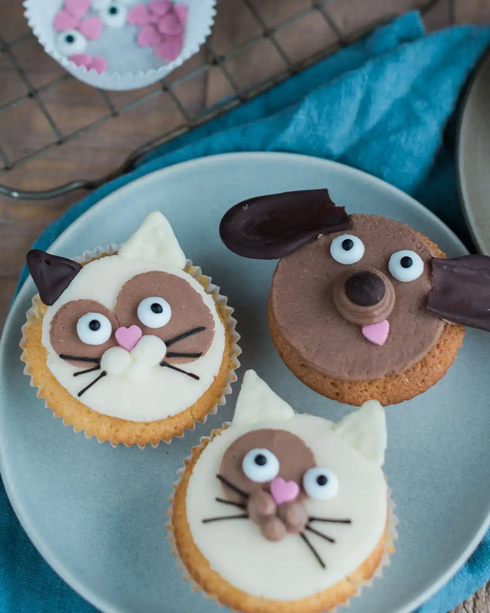 Honeywell Bakes Cat & Dog Cupcake Baking Kit - Cupcakes decorated to look like dogs on a wooden table with a bowl of chocolate frosting.