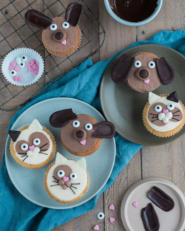 Honeywell Bakes Cat & Dog Cupcake Baking Kit - Cupcakes decorated like dogs and cats on a wooden table with a blue cloth.