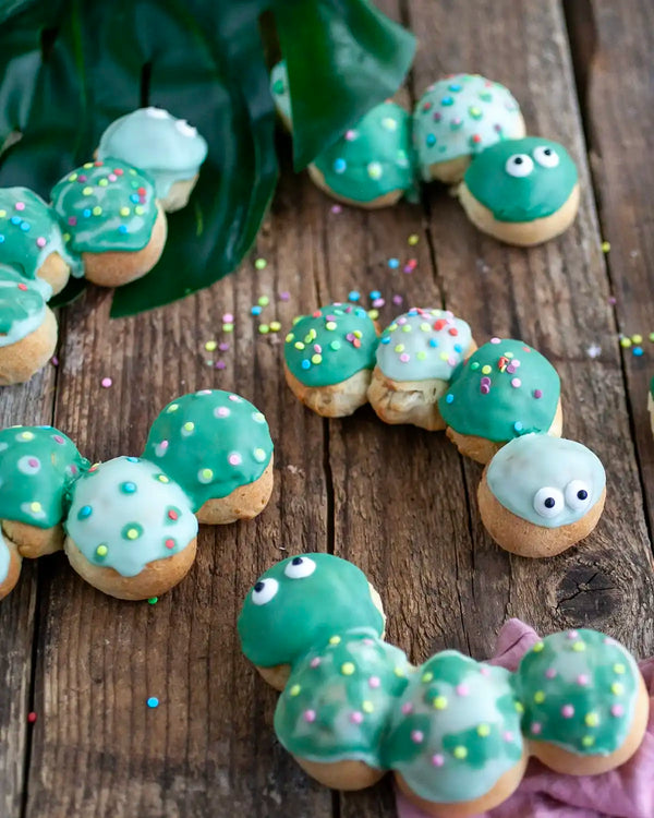 Honeywell Bakes Caterpillar Iced Bun Baking Kit - Decorative iced buns shaped like caterpillars with green bodies and faces on a wooden surface.