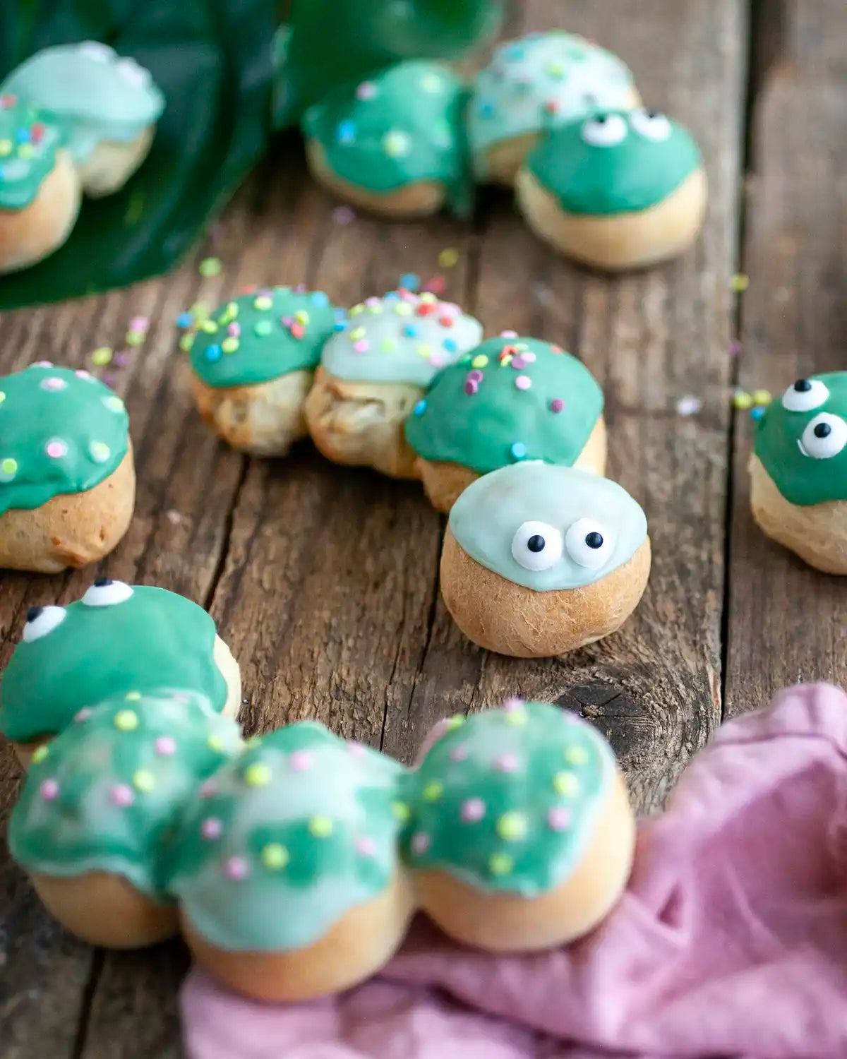 Honeywell Bakes Caterpillar Iced Bun Baking Kit - Decorative iced buns shaped like caterpillars with green bodies and faces on a wooden surface.