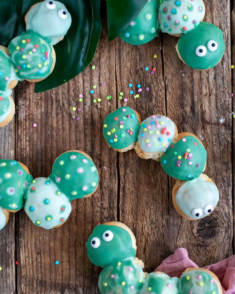 Honeywell Bakes Caterpillar Iced Bun Baking Kit - Decorative iced buns shaped like caterpillars with green bodies and faces on a wooden surface.