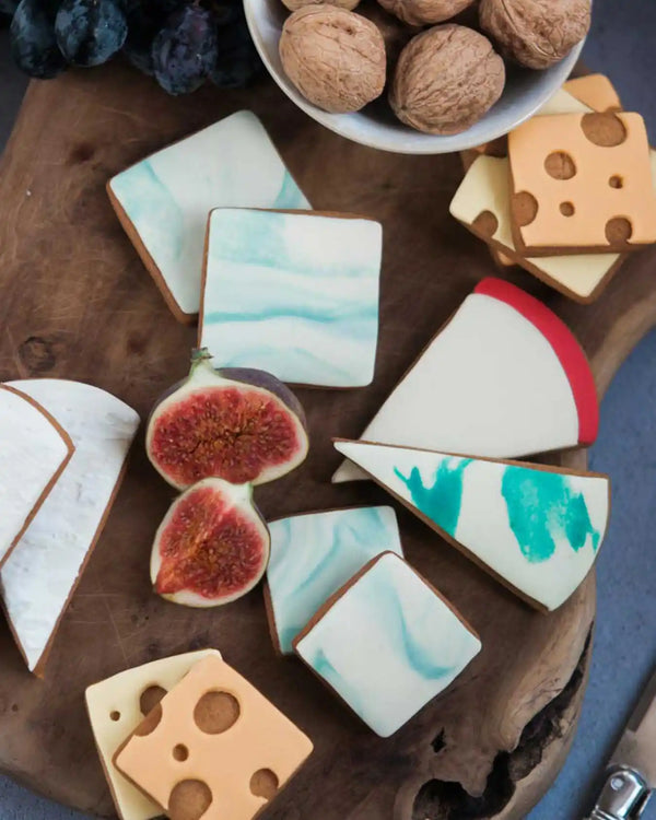 Honeywell Bakes Cheese Biscuit Gift Set - Decorative cookies shaped like cheese, figs, and bread on a wooden board with a bowl of nuts.