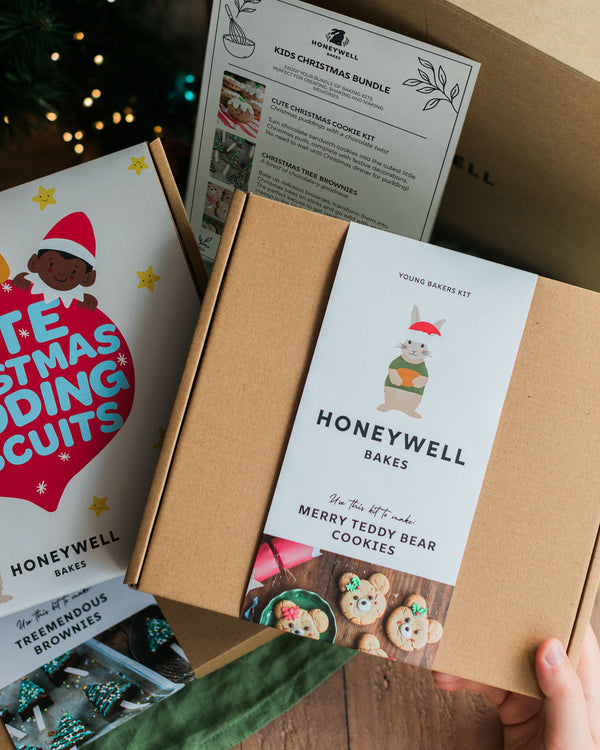 The Children’s Christmas Baking Bundle by Honeywell Bakes, featuring three festive baking kits for kids: Christmas pudding biscuits, Christmas tree brownies and teddy bear cookies, shown in their gift packaging beside a Christmas tree.