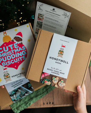 The Children’s Christmas Baking Bundle by Honeywell Bakes, featuring three festive baking kits for kids: Christmas pudding biscuits, Christmas tree brownies and teddy bear cookies, shown in their gift packaging beside a Christmas tree.