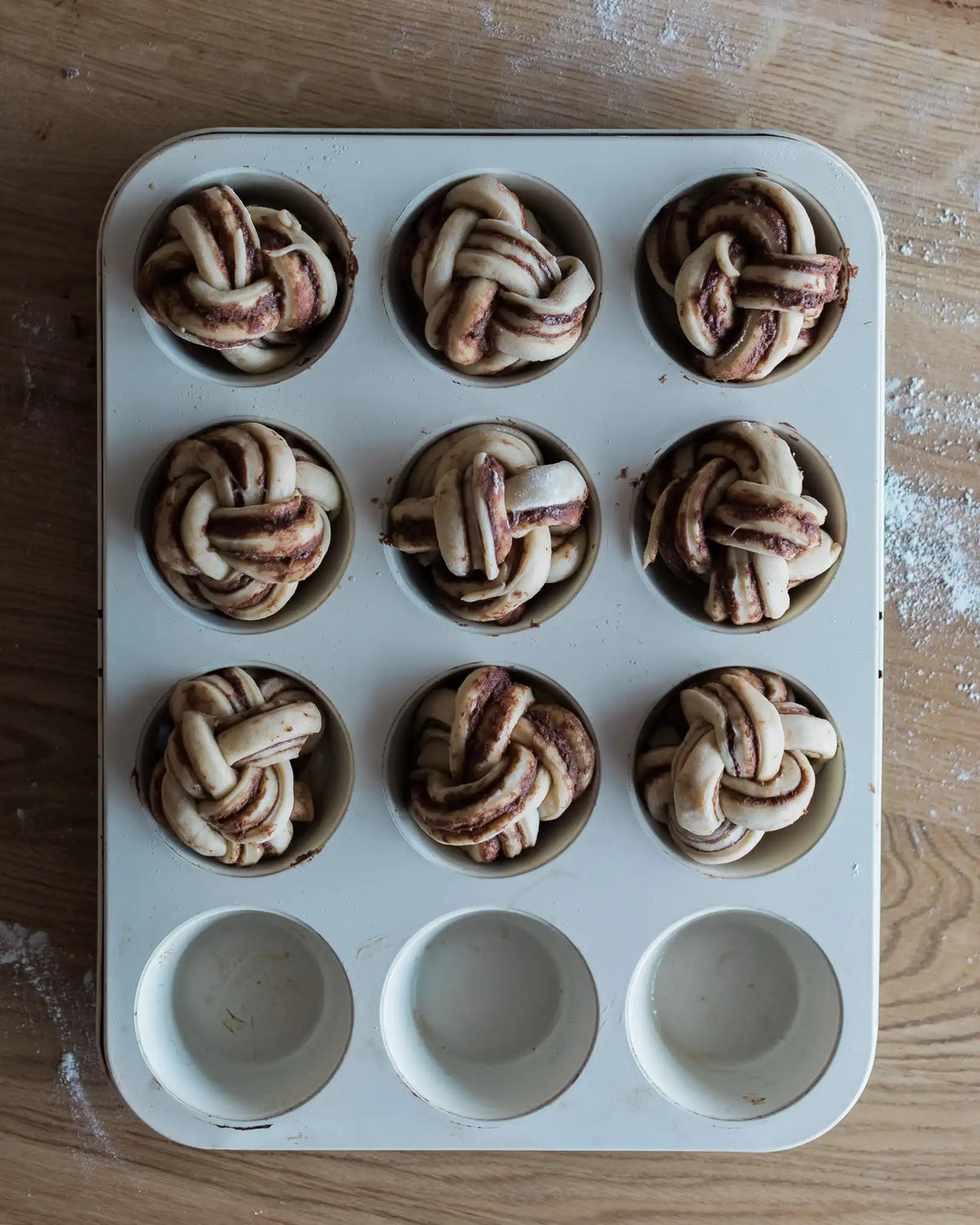 Honeywell Bakes Chocolate & Hazelnut Babka Buns - Muffin tin with unbaked bread rolls on a wooden surface