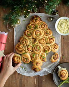 Honeywell Bakes - A tree-shaped bread arrangement made of rolled dough pieces with rosemary sprigs, served on parchment paper on a wooden table with holiday decorations, a dipping sauce bowl, and a hand reaching in.