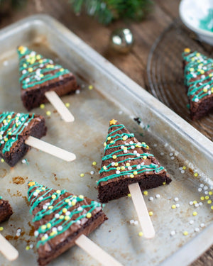 Honeywell Bakes Christmas Tree Brownie Baking Kit, Tree-shaped brownie pops decorated with green icing and colourful sprinkles, arranged on a metal baking sheet.