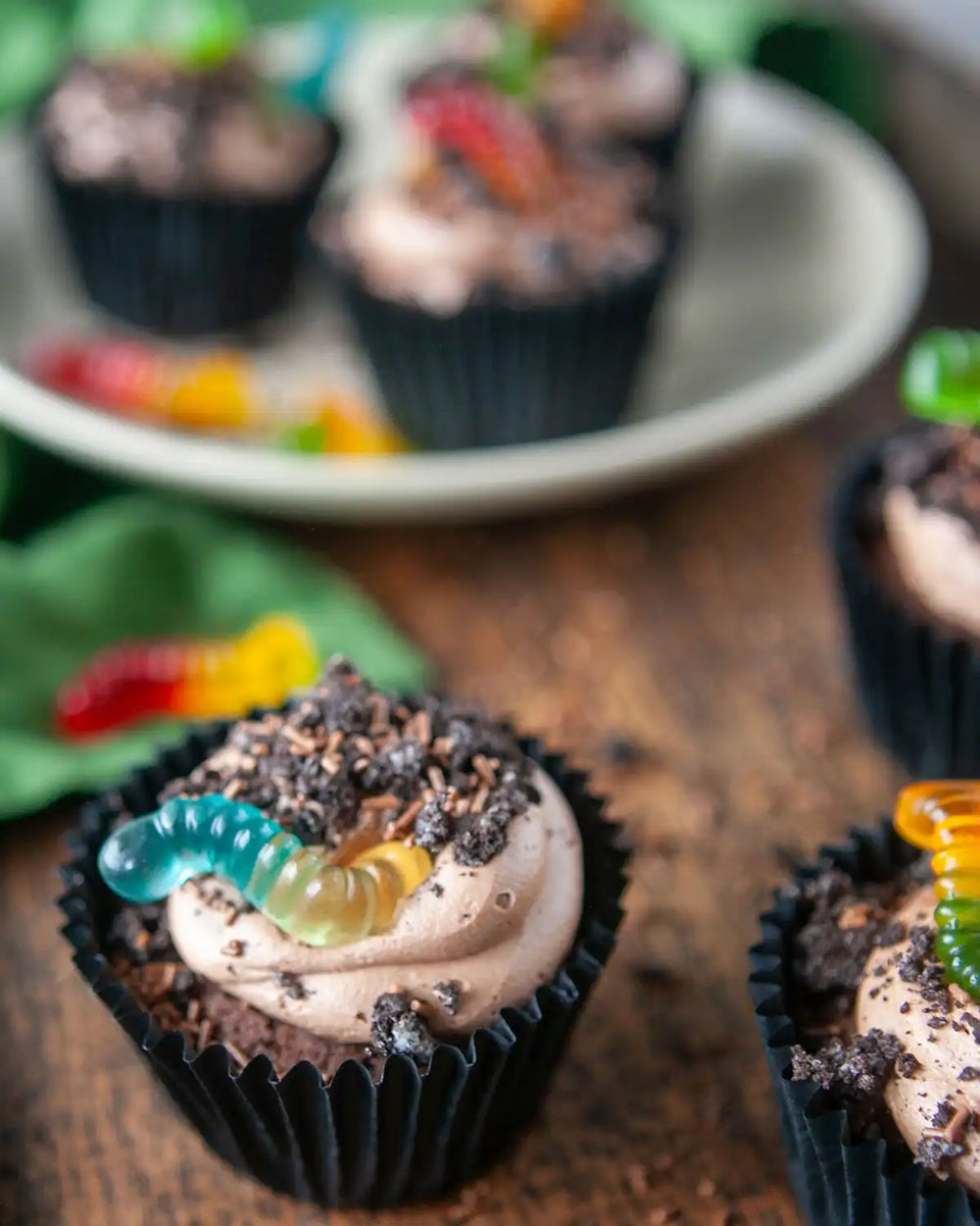 Honeywell Bakes Creepy Crawly Cupcake Baking Kit - Chocolate cupcakes with gummy worms on a wooden surface and plate.