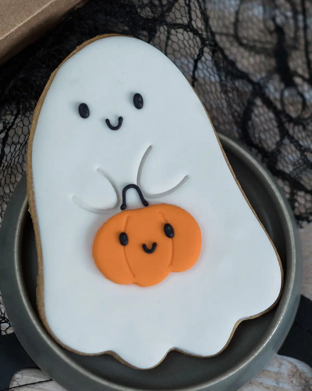 Honeywell Bakes Cute Ghost Biscuit - Ghost-shaped cookie with a pumpkin on a black lace background