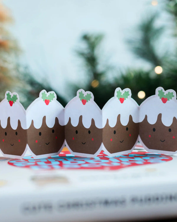 A row of cute, cut out Christmas pudding paper cutouts from Christmas pudding sandwich biscuit baking kit packaging made by Honeywell Bakes