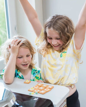 Honeywell Bakes DIY Noughts and Crosses Biscuit Game - Two children  playing with tic-tac-toe cookies on a tray indoors.
