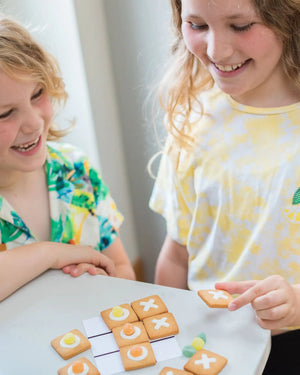 Honeywell Bakes DIY Noughts and Crosses Biscuit Game - Two children playing with a game of cookies on a table.