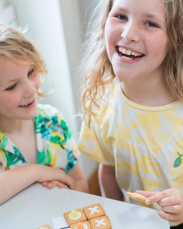 Honeywell Bakes DIY Noughts and Crosses Biscuit Game - Two children sitting at a table with cookies, smiling and enjoying each other's company.