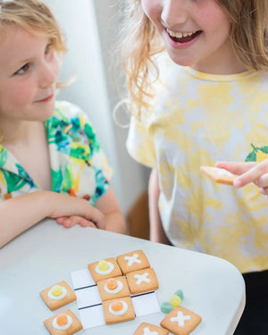 Honeywell Bakes DIY Noughts and Crosses Biscuit Game - Two children playing with cookies shaped like a tic-tac-toe game on a table.