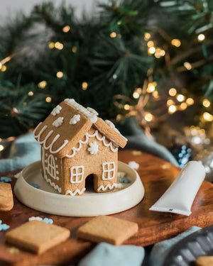 Honeywell Bakes DIY Tiny Gingerbread House Kit - biscuit gingerbread house on a wooden plate with icing tube and biscuits