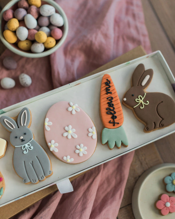Honeywell Bakes Easter Egg Hunt Biscuit Gift - Decorative cookies shaped like bunnies, eggs, and carrots on a tray with a pink cloth background.