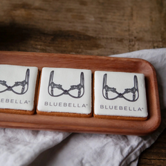 Three cookies finished with edible ink printed branding, with 'BLUEBELLA' logo branding on a wooden board.