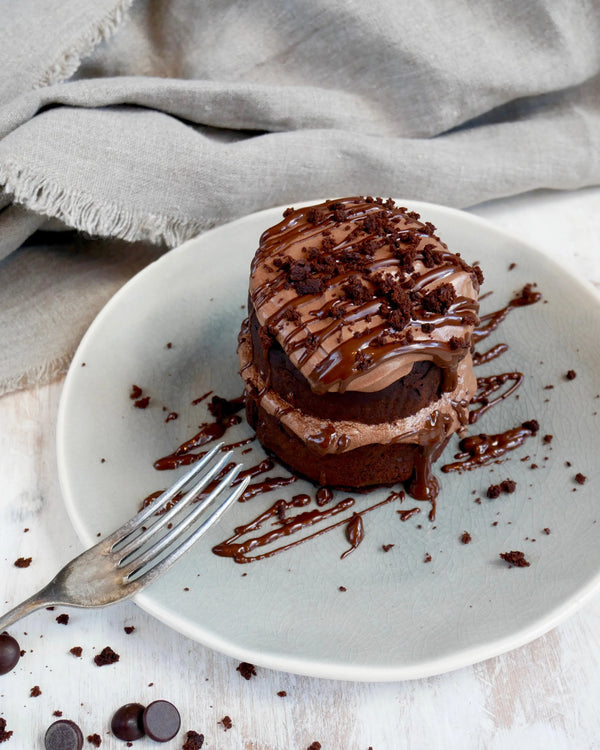 Honeywell Bakes Emergency Chocolate Cake Kit - Chocolate cake on a white plate with a fork, surrounded by chocolate pieces and a grey cloth.