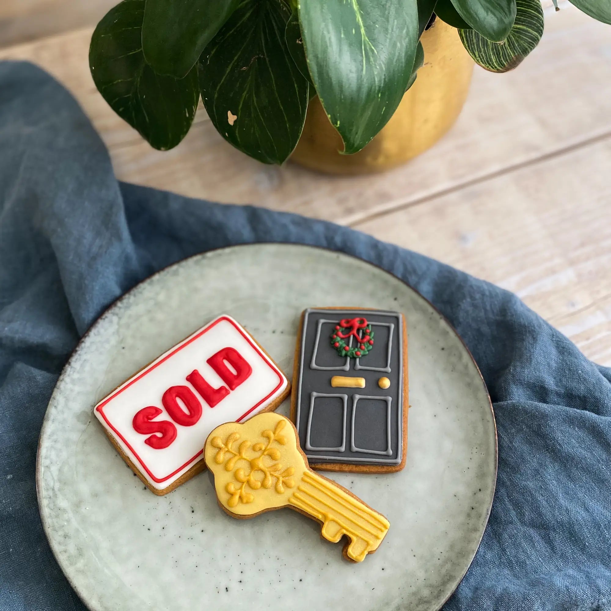Honeywell Bakes biscuits for Estate Agent Property gifting, Three decorated sugar cookies shaped like a 'SOLD' sign, a gray front door with a wreath, and a gold key.