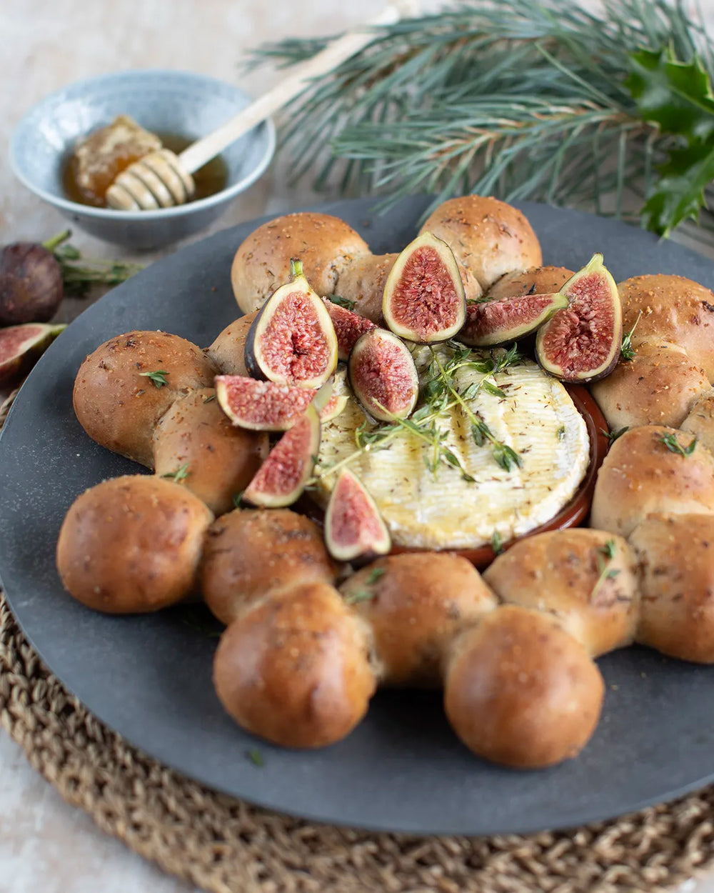 Honeywell Bakes Fig and Walnut Bread Wreath Baking Kit - Baked camembert with figs and bread rolls on a dark plate with a bowl of honey and a stick in the background.