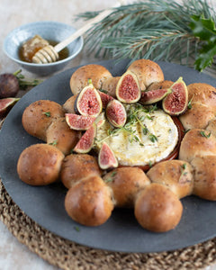 Honeywell Bakes Fig and Walnut Bread Wreath Baking Kit - Baked camembert with figs and bread rolls on a dark plate with a bowl of honey and a stick in the background.