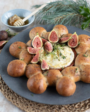 Honeywell Bakes Fig and Walnut Bread Wreath Baking Kit - Baked camembert with figs and bread rolls on a dark plate with a bowl of honey and a stick in the background.