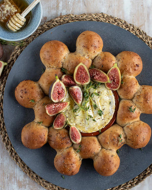 Honeywell Bakes Fig and Walnut Bread Wreath Baking Kit - Baked camembert with figs and bread rolls on a dark plate with a bowl of honey and a stick in the background.