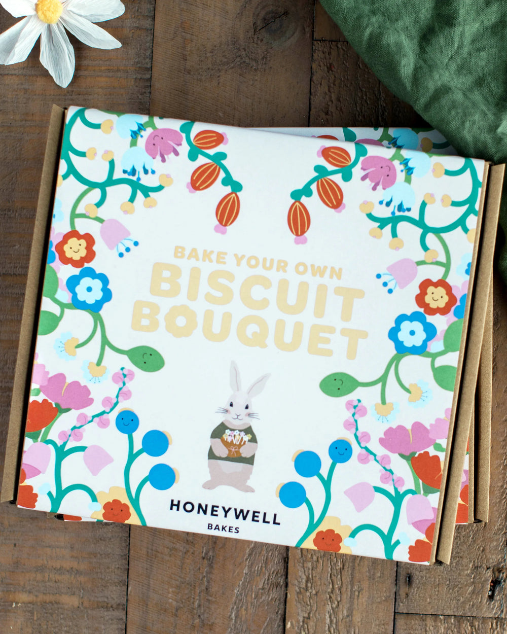 Honeywell Bakes Flower Biscuit Pops Baking Kit - Decorative cookies shaped like flowers on sticks arranged on a wooden board with a green cloth background.