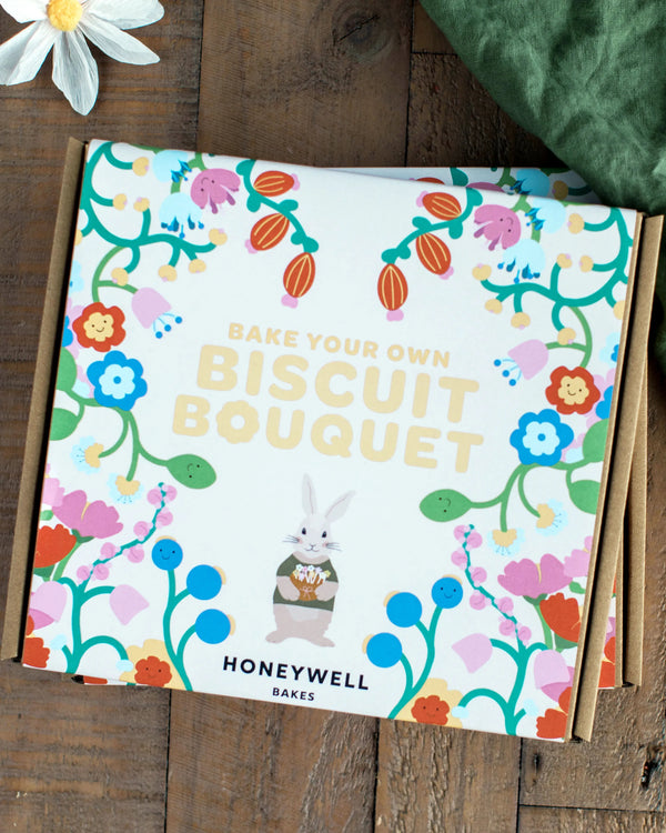 Honeywell Bakes 'Bake Your Own Biscuit Bouquet' kit on a wooden surface with flowers and a green cloth.