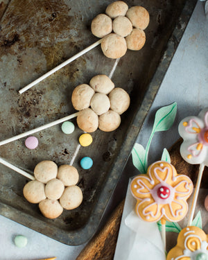 Honeywell Bakes Flower Biscuit Pops Baking Kit - Decorative cookies on sticks with colourful smarties and a floral design on a baking tray.