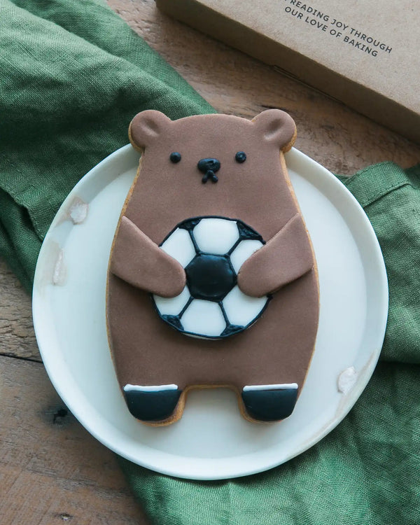 Honeywell Bakes Football Biscuit Bear - Cookie shaped like a bear holding a football on a white plate with a green cloth in the background.