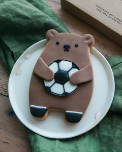Honeywell Bakes Football Biscuit Bear - Cookie shaped like a bear holding a football on a white plate with a green cloth in the background.