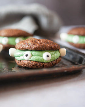 Honeywell Bakes Young Bakers Subscription, a sandwich cookie designed to look like a cartoon monster, with brown cookie layers, bright green frosting, with edible eyes