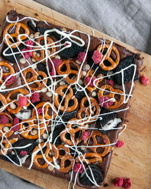 Honeywell Bakes Fully Loaded Brownie Baking Kit - Brownie bar with pretzels, cookies, and white chocolate drizzle on a wooden board.